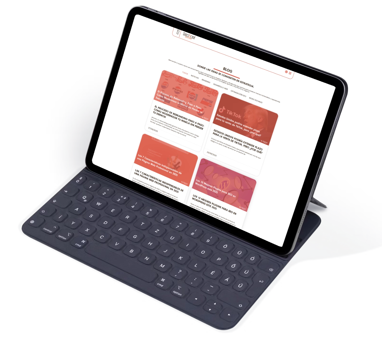 Una tableta con teclado negro muestra una página de blog con cuatro avances de artículos en rojo y blanco, que incluyen temas como cuánto cuesta un branding profesional en México. La cuadrícula muestra el título, la imagen y la descripción de cada artículo.